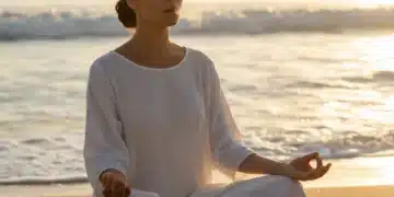 Woman meditating on beach, practicing breathing techniques for calm.