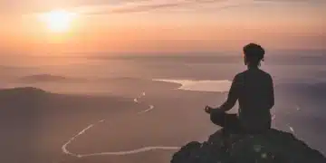 Person meditating on a mountain at sunrise, symbolizing intentional living and peace.